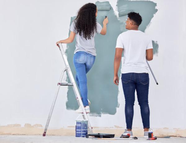 A young couple paints a wall inside a home teal color