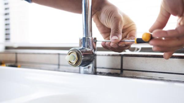 A man fixes a leaking faucet with a screwdriver.